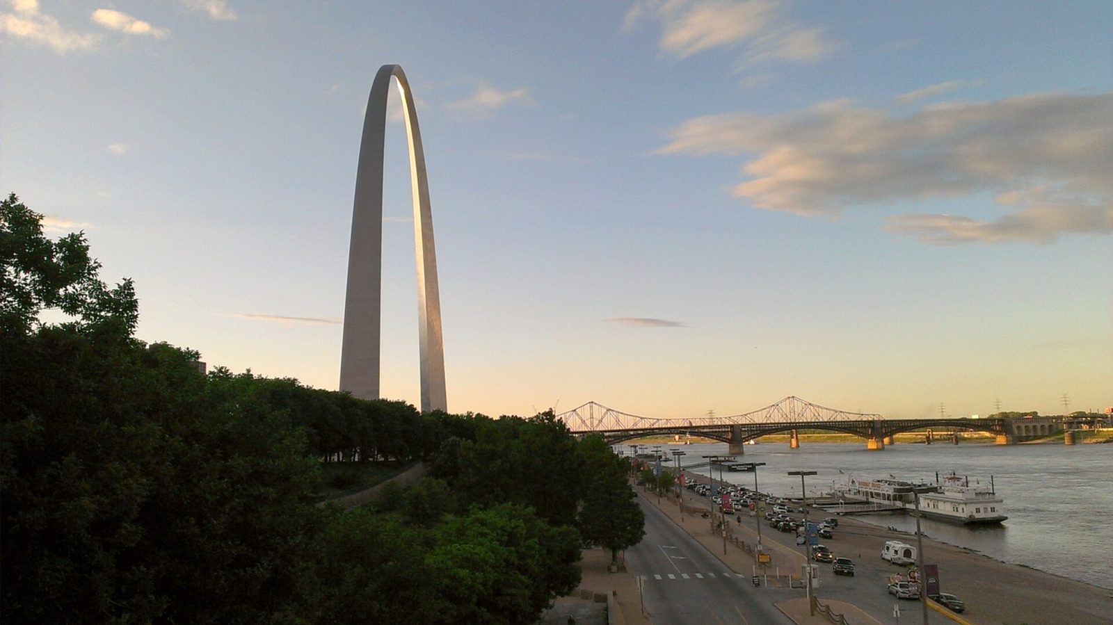 The Gateway Arch above the St. Louis riverfront at evening, with Eads Bridge behind.