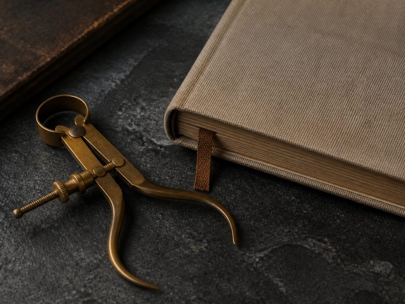 A brass caliper beside a cloth-bound notebook on a slate table.